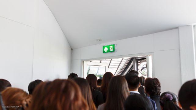 Many people walk toward a door marked as an emergency exit