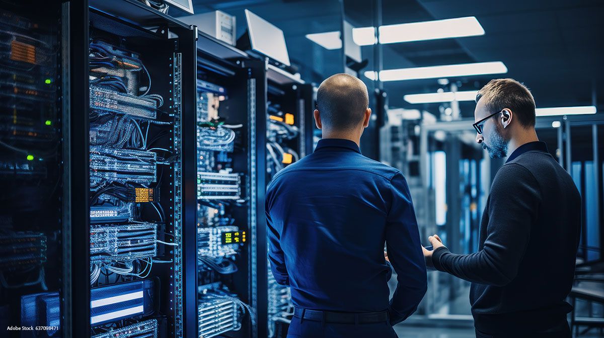 Two men are standing in a dark blue server room
