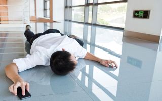 Mann liegt bäuchlings auf dem Boden eines Flurs mit einem Smartphone in der rechten Hand