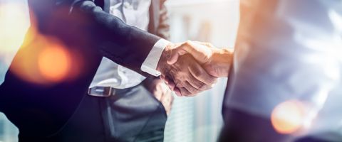 Two businessmen shaking hands; only their cores a visible in the frame