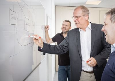 Four people in front of a whiteboard, one of them drawing a diagram