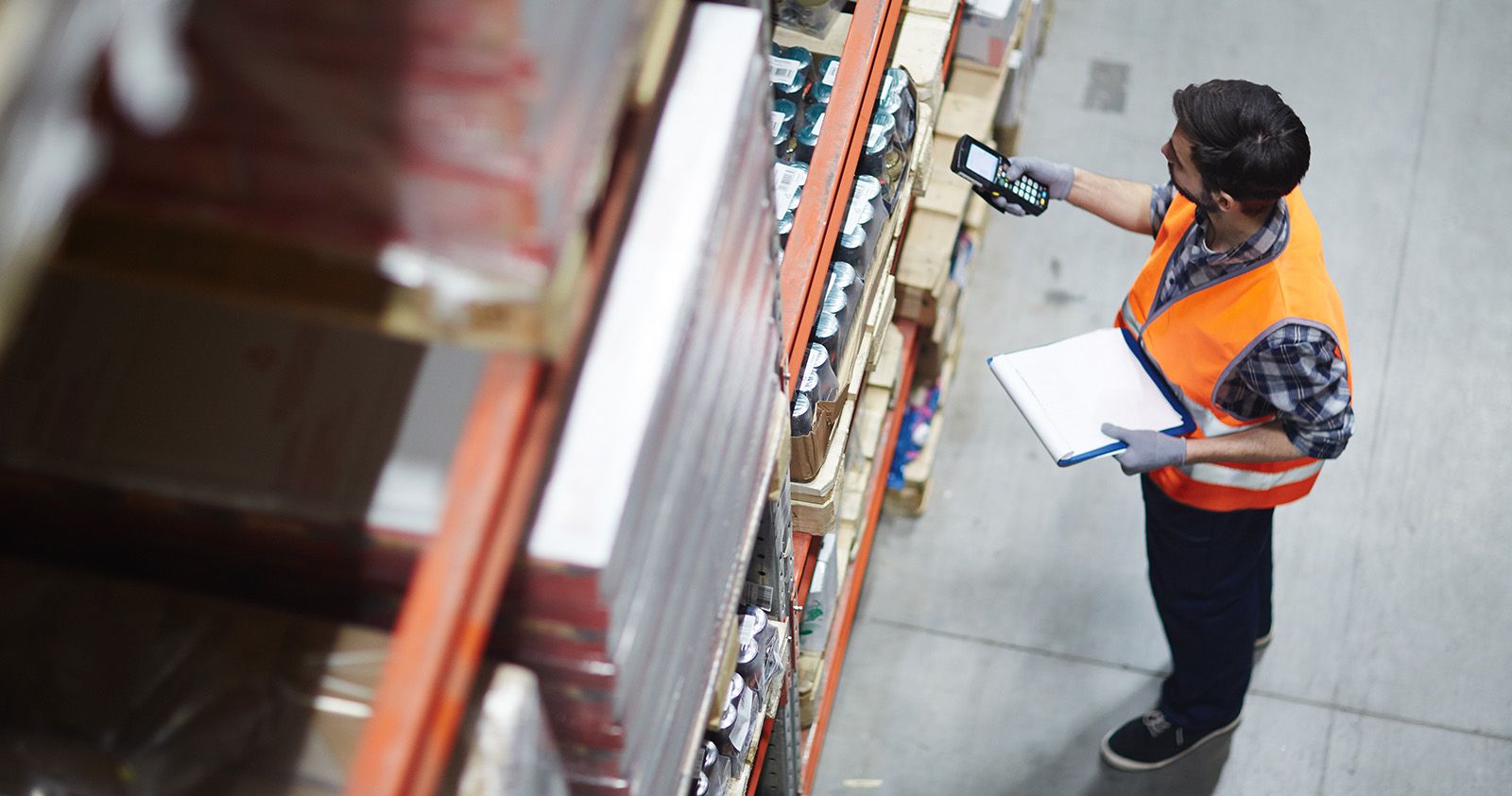 Man with orange high-visibility vest shot diagonally from above scanning goods in a high rack