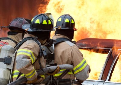 Three firefighters from behind extinguishing a vehicle fire