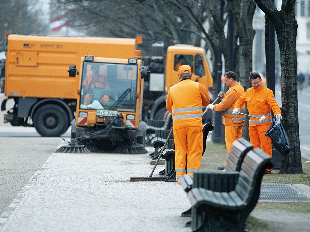 Foto von orangen Reinigungsfahrzeugen und orange gekleideten Mitarbeitern der Berliner Stadtreinigung